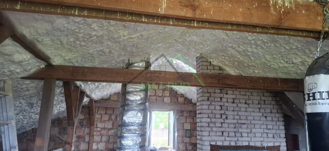 Płatew i słupy więźby na tle ocieplonego dachu, w ścianie szczytowej okno